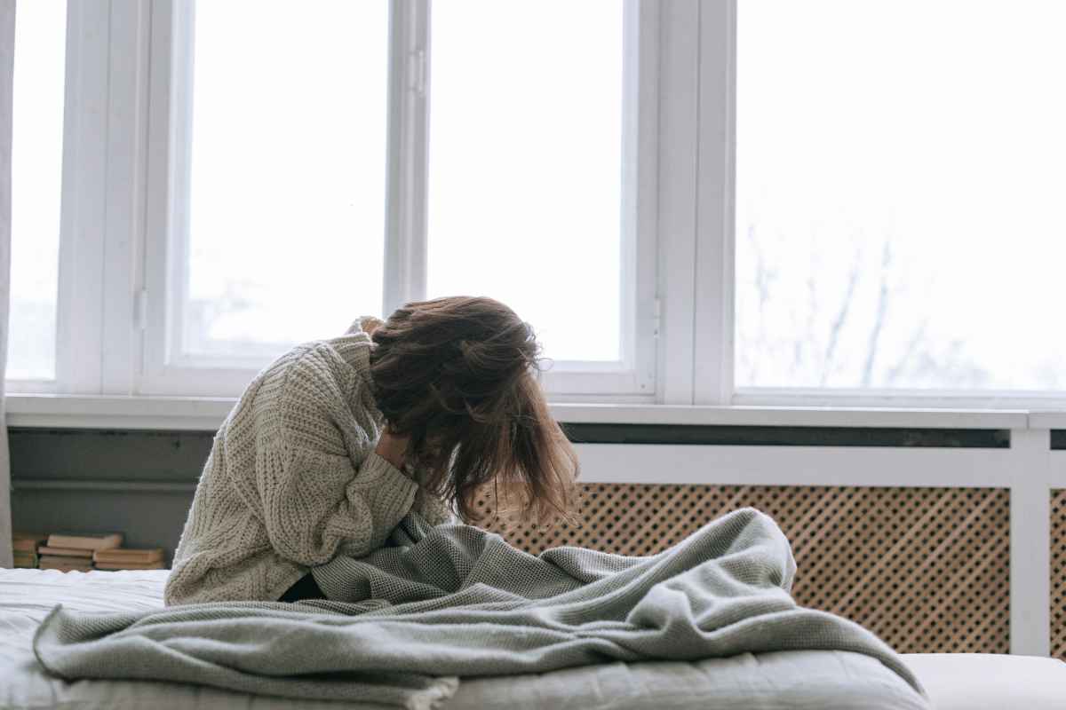 persona sul letto con la testa tra le mani