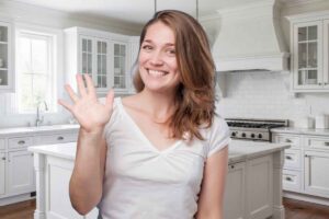 una donna fa ciao con la mano davanti a una cucina tinteggiata di bianco