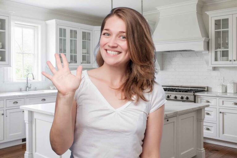 una donna fa ciao con la mano davanti a una cucina tinteggiata di bianco