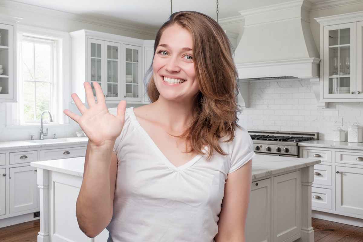 una donna fa ciao con la mano davanti a una cucina tinteggiata di bianco