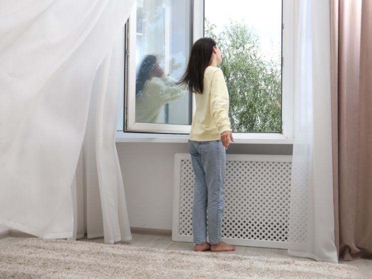 donna davanti ad una finestra aperta in casa