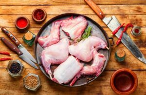 carne di coniglio in tegame, coltelli e spezie su tagliere di legno
