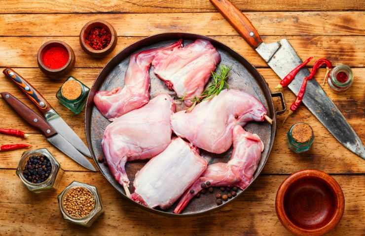 carne di coniglio in tegame, coltelli e spezie su tagliere di legno