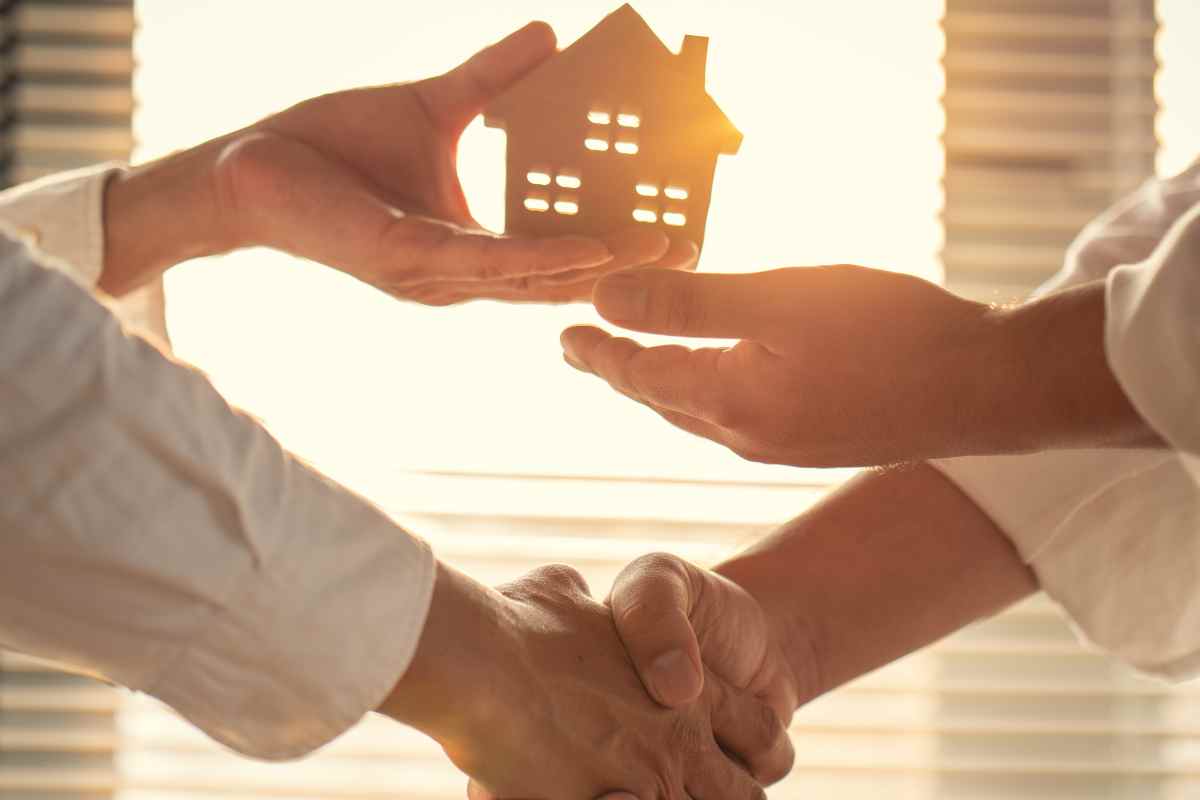 due mani si stringono e tengono una miniatura di una casa