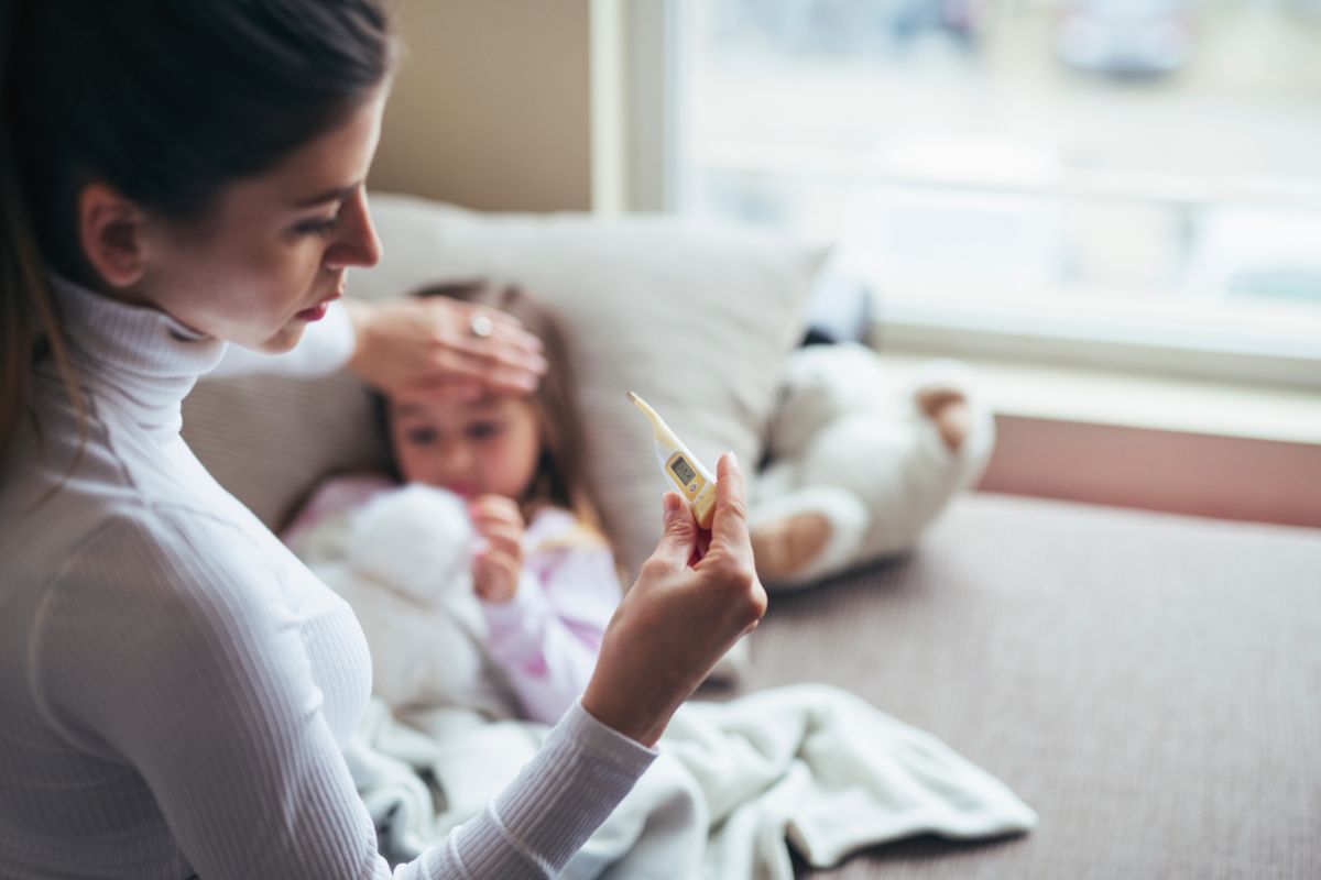 mamma con termometro in mano e con l'altra tocca fronte della figlia malata