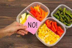 contenitori di plastica con delle verdure dentro e mano che mantiene un post-it con la scritta no