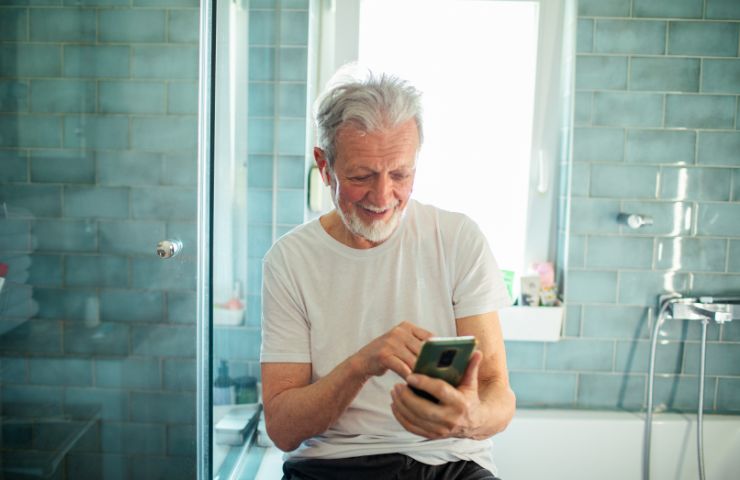 uomo anziano con smartphone in bagno
