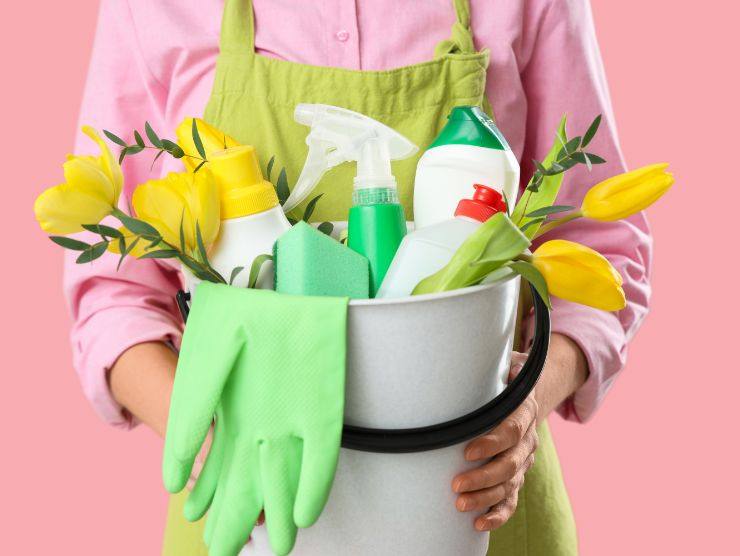 donna che mantiene secchio con prodotti per la pulizia con dei fiori dentro