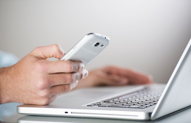 uomo al pc con smartphone in mano